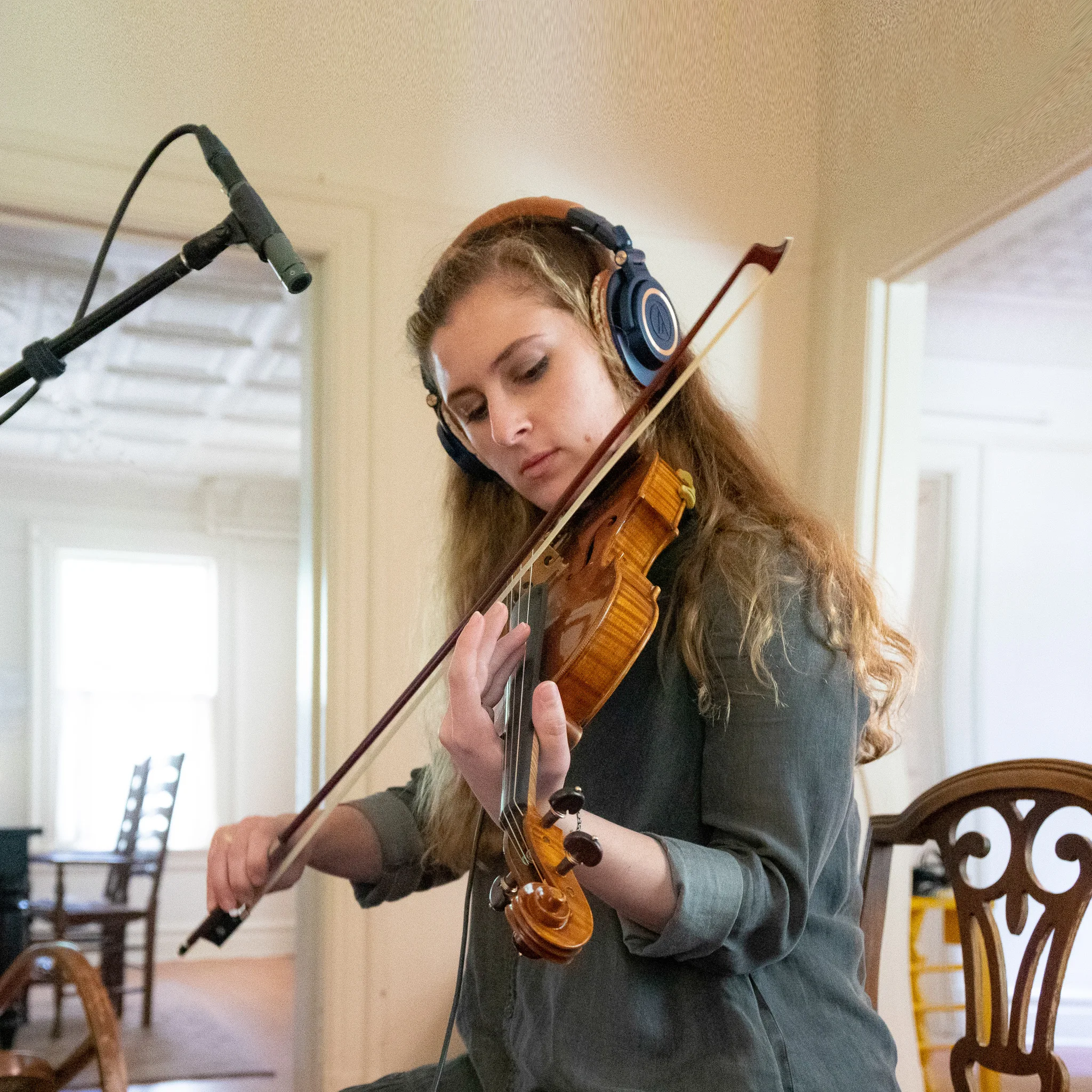 Honor Monaco playing violin in her home studio, wearing headphones with a microphone beside her